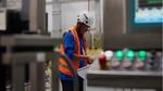Ein Mitarbeiter in Sicherheitskleidung bedient eine Maschine in einen Fabrik.